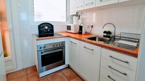A compact kitchen with a stove, oven, microwave, sink, and white cabinets. - Apartment Cabrera Burriac (Cabrera de Mar)