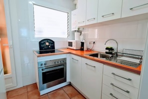 A compact kitchen with a stove, oven, microwave, sink, and white cabinets.