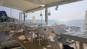 An outdoor seating area with tables and chairs, a covered section, and a view of the sea. - Apartment Cabrera Burriac (Cabrera de Mar)