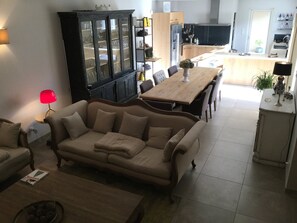 Uma sala de estar com sofá, mesa de jantar e cozinha ao fundo.