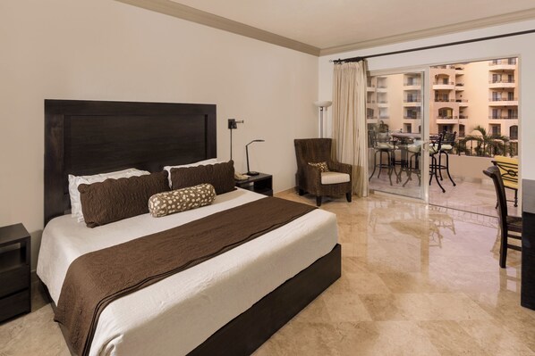 Une chambre d’hôtel avec un grand lit, une chaise, un bureau et un balcon donnant sur d’autres immeubles.
