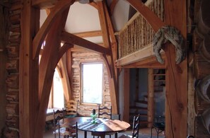 Ein rustikaler Essbereich aus Holz mit einem runden Tisch und Stühlen, einer Steinwand und einem großen Fenster, das viel Tageslicht hereinlässt.