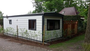 Un pequeño edificio de una sola planta con fachada blanca y detalles negros, que cuenta con dos ventanas y una puerta pequeña.