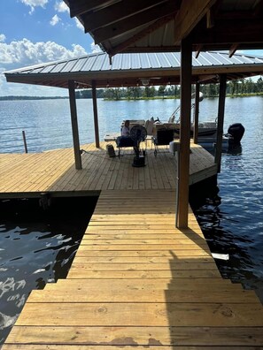 A wooden dock extending into a calm lake, with a covered seating area and a boat docked nearby. - Get away to beautiful Caney Lake!  (Chatham)