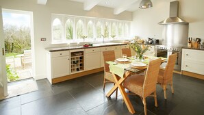 A modern kitchen with a large island, white cabinetry, and a view of the garden through the windows. - Woodland Cottage, South Moulton, a beautiful, spacious cottage on two floors in a private location (South Molton)