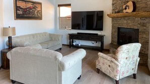 Una sala de estar con sofá, sillón, televisión y chimenea.