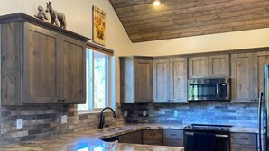 Una cocina moderna con armarios de madera, una isla de granito, electrodomésticos de acero inoxidable y un techo alto.