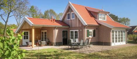 Et toetagers hus med rødt tegltag, murstensfacade og en overdækket terrasse med udendørs møbler.