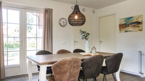 Un coin repas avec une table en bois, six chaises, un luminaire suspendu, une horloge, un vase avec des fleurs et un tableau au mur.