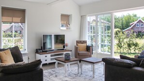 Un salon moderne doté d’un téléviseur à écran plat, de sièges confortables et de grandes fenêtres offrant une vue sur les environs.
