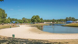 Une zone de plage sablonneuse avec un étang, des arbres et des tentes.
