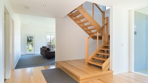 Un intérieur moderne avec un escalier en bois, une moquette grise et un canapé dans une pièce lumineuse dotée de grandes fenêtres.