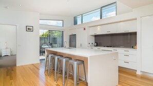 Une cuisine moderne dotée d’un grand îlot central, d’appareils électroménagers en acier inoxydable et offrant une vue sur l’extérieur.