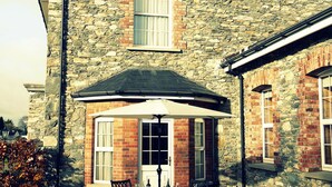 A stone building with a curved bay window, a patio with outdoor furniture, and a chimney. - Large Luxury House in Excellent Location. Ideal for families  (Killarney)