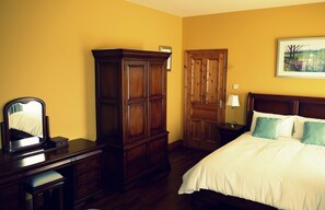 Un dormitorio con un armario de madera, una mesita de noche con lámpara y una cama con almohadas.