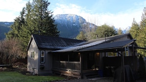 Eine kleine Holzhütte mit Veranda, umgeben von Bäumen und Bergen.