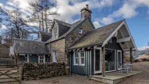 A stone house with a sloped roof, a chimney, and a small porch with outdoor seating. - Beautiful Sky Cottage overlooking Loch Tay (Aberfeldy)