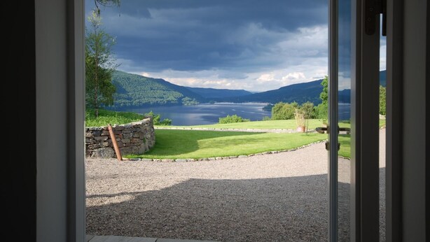 A view of a lake with surrounding hills, a stone wall, and a gravel path leading to a door. - Beautiful Sky Cottage overlooking Loch Tay (Aberfeldy)