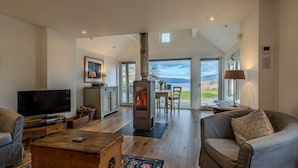 A spacious living room with a large fireplace, a television, and a view of the outdoors. - Beautiful Sky Cottage overlooking Loch Tay (Aberfeldy)