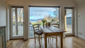 A dining area with a wooden table and chairs, a bottle of wine, and a vase of flowers. - Beautiful Sky Cottage overlooking Loch Tay (Aberfeldy)