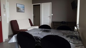 A dining area with a table, chairs, a sofa, and a door. - Apartment n°4 (2/4 P.) on 2nd floor without elevator (Berck-sur-mer)