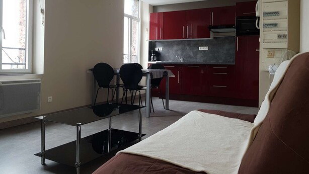 A compact kitchen with red cabinets, a black countertop, and a small dining area with two chairs. - Apartment n°4 (2/4 P.) on 2nd floor without elevator (Berck-sur-mer)