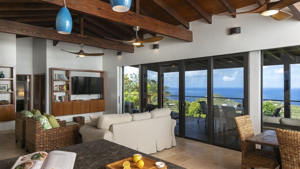 A modern living room with a large window, a dining area, and a kitchen with a marble countertop. - Eureka Villa! Stunning Views in Paradise! 3BR, 3.5BA (Rendezvous Bay)