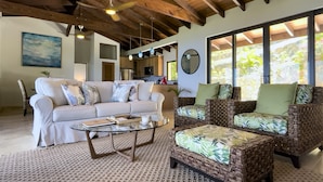 A spacious living area with a high ceiling, a sofa set, a coffee table, and a view of the outdoors through large windows. - Eureka Villa! Stunning Views in Paradise! 3BR, 3.5BA (Rendezvous Bay)