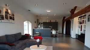 Ein modernes Wohnzimmer mit einem grauen Sofa, einem weißen Couchtisch und einer Küche im Hintergrund.