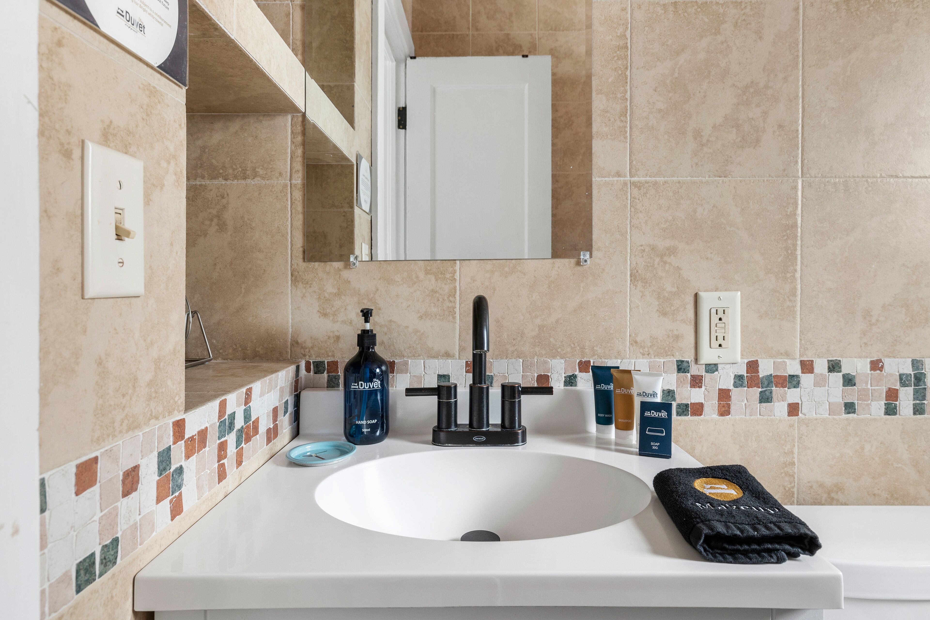 A bathroom with a white sink, a black faucet, a bottle of hand soap, a towel, and a mirror above the sink.