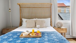 Een slaapkamer met een bed, een dienblad met ontbijt, een nachtkastje en een raam met gordijnen.