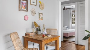 Een eetgedeelte met een houten tafel, rieten stoelen en wanddecoraties, waaronder een lijstwerk met kunst en een geweven mand.