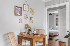 Un coin repas avec une table en bois, des chaises en osier et des décorations murales, notamment des œuvres d’art encadrées et un panier tressé.