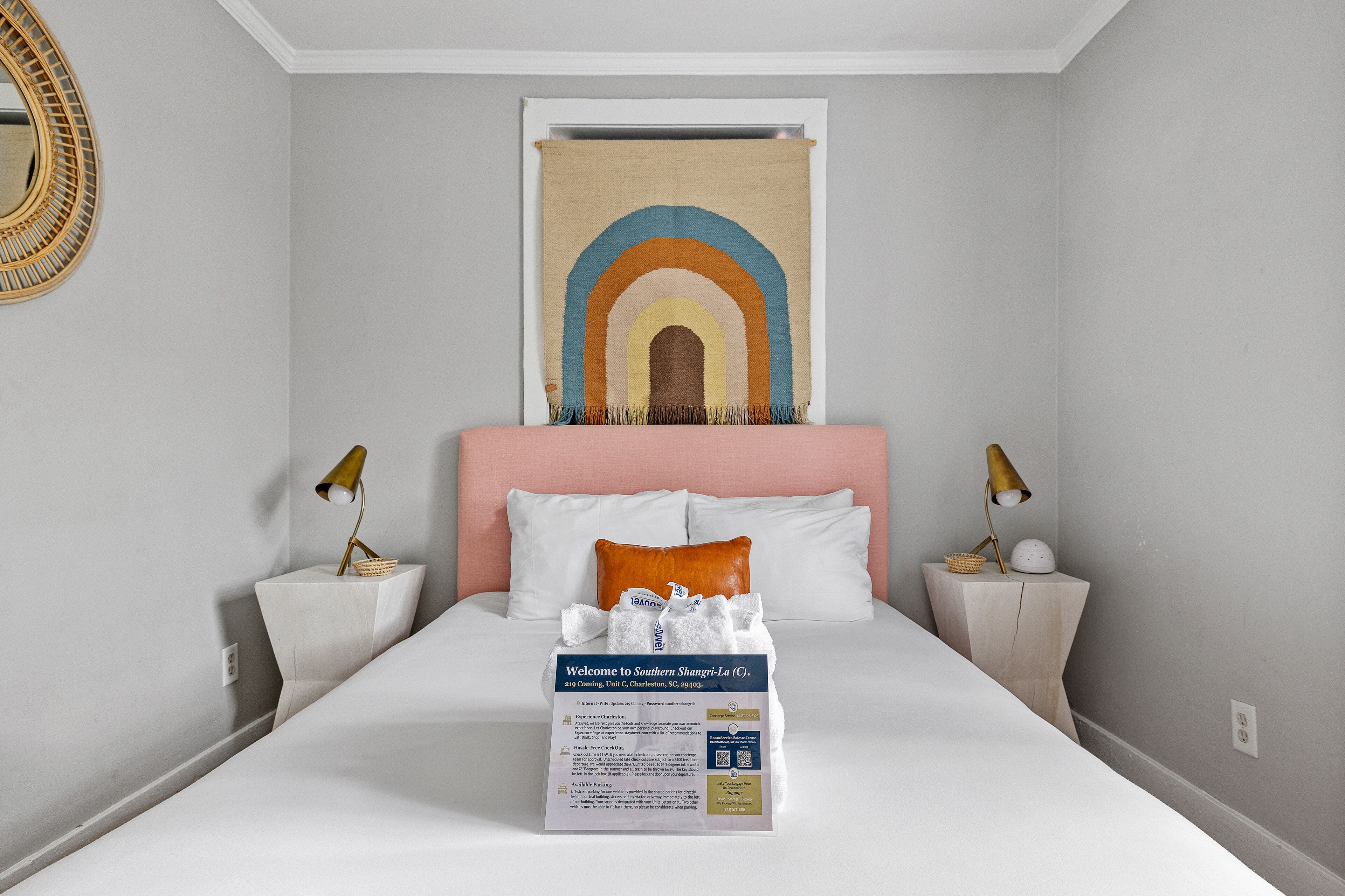 A hotel room with a bed, two bedside tables, a headboard with a rainbow tapestry, and a welcome sign.