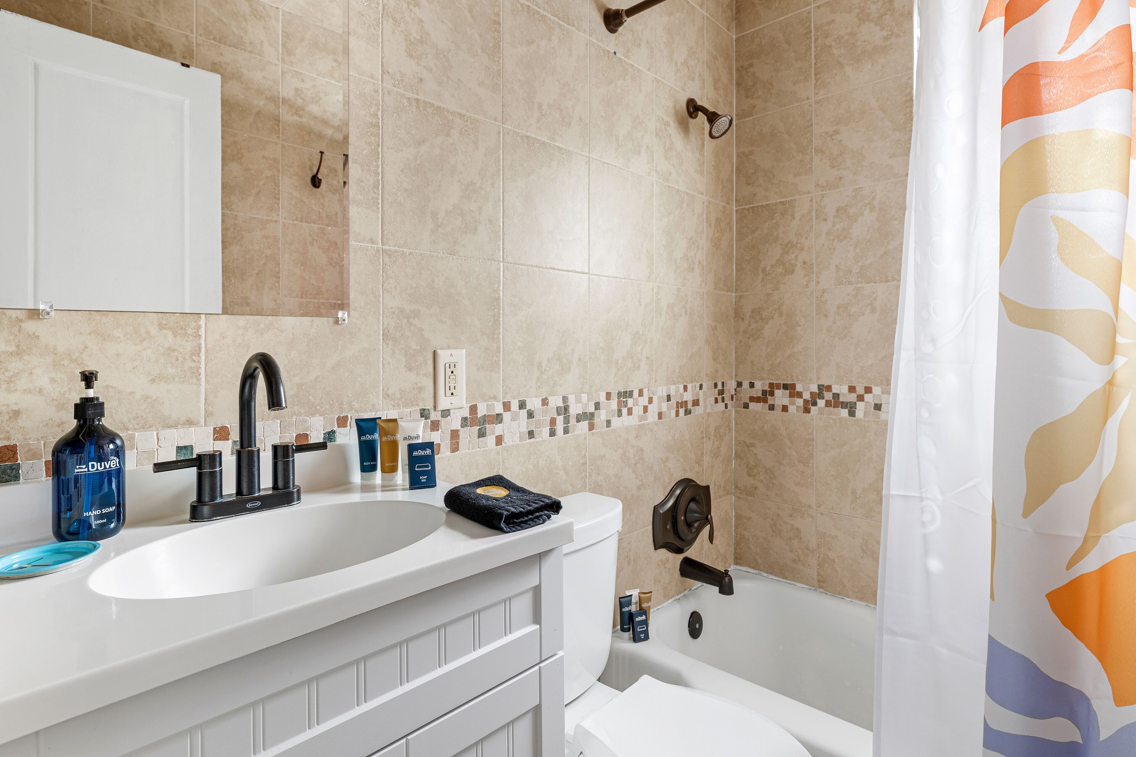 Un bagno con un lavandino bianco, un rubinetto nero e una tenda da doccia con motivo floreale.