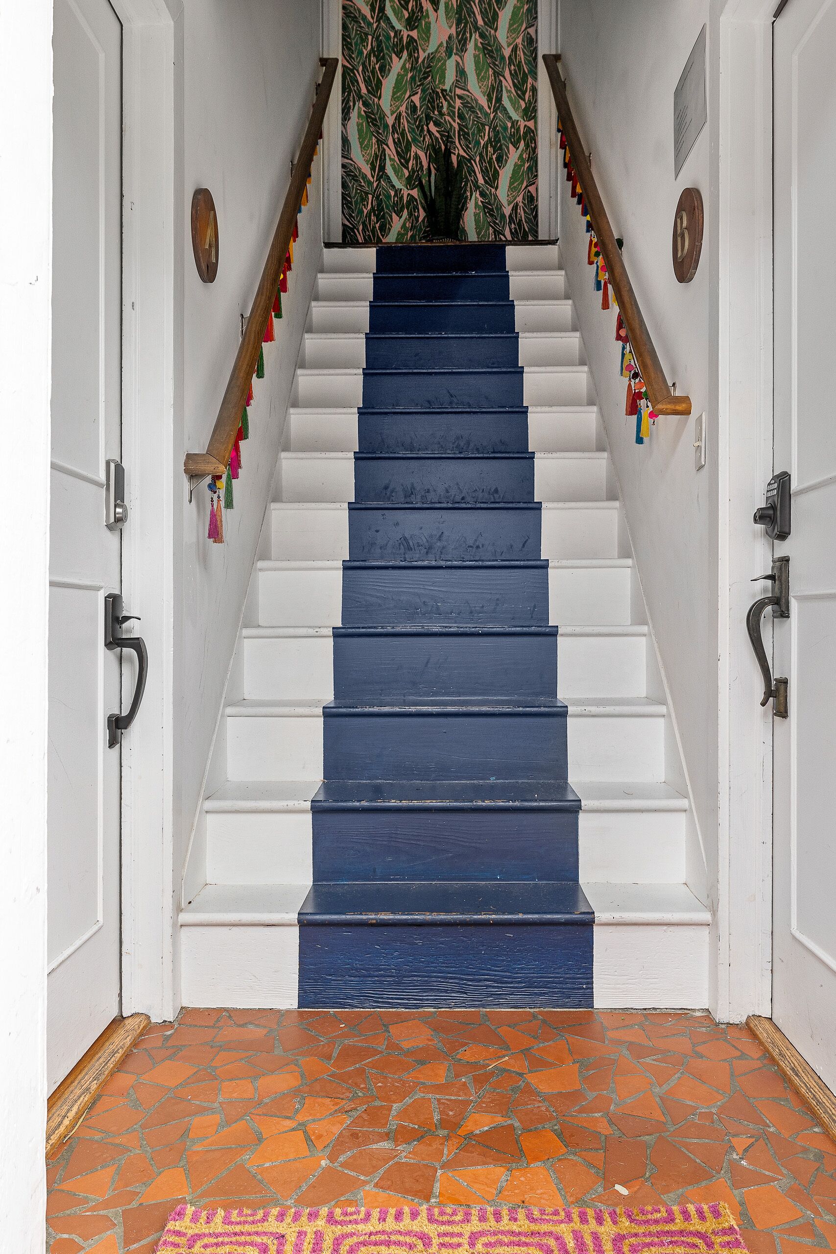 A staircase with alternating white and blue steps, a wooden handrail, and a patterned wall at the top.