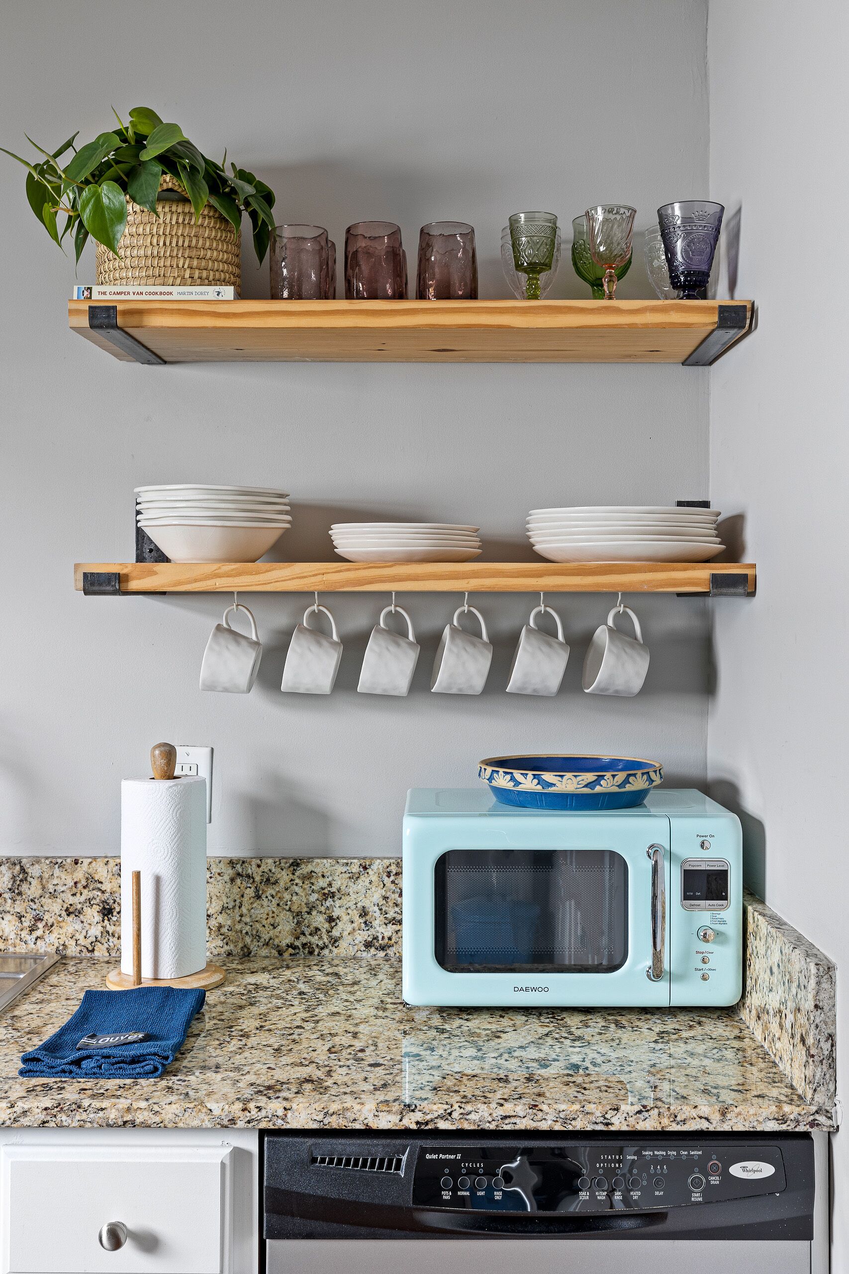 Una cocina con microondas, escurreplatos y un juego de tazas colgadas.