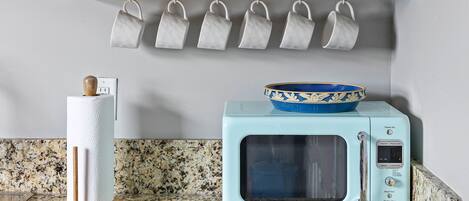 Una cocina con microondas, escurreplatos y un juego de tazas colgadas.