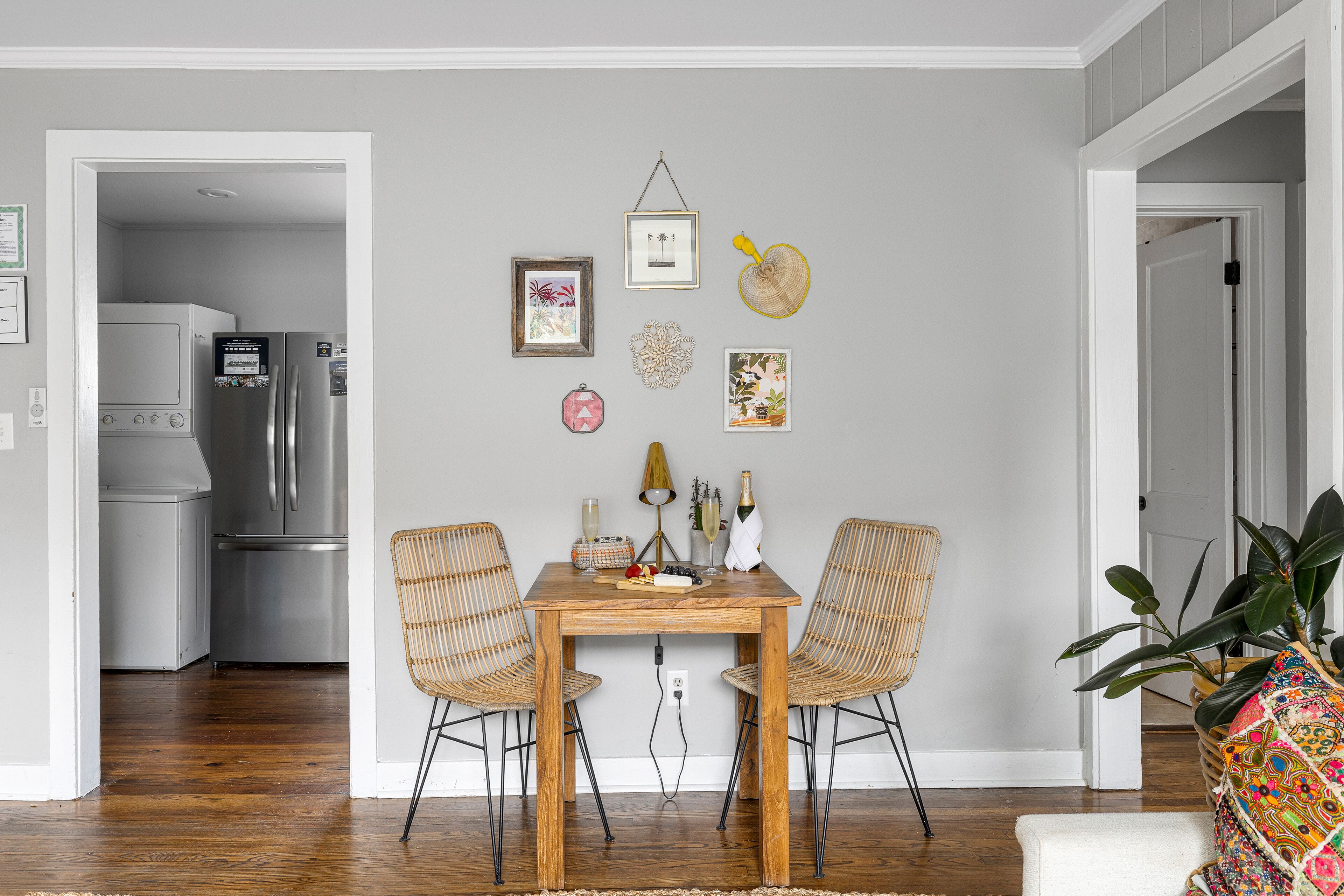 A dining area with a wooden table and two wicker chairs, a kitchen with stainless steel appliances, and a potted plant.