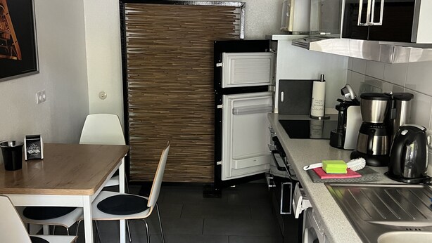 Cocina compacta con zona de comedor, que incluye una mesa, sillas, refrigerador, microondas, hervidor y cafetera.