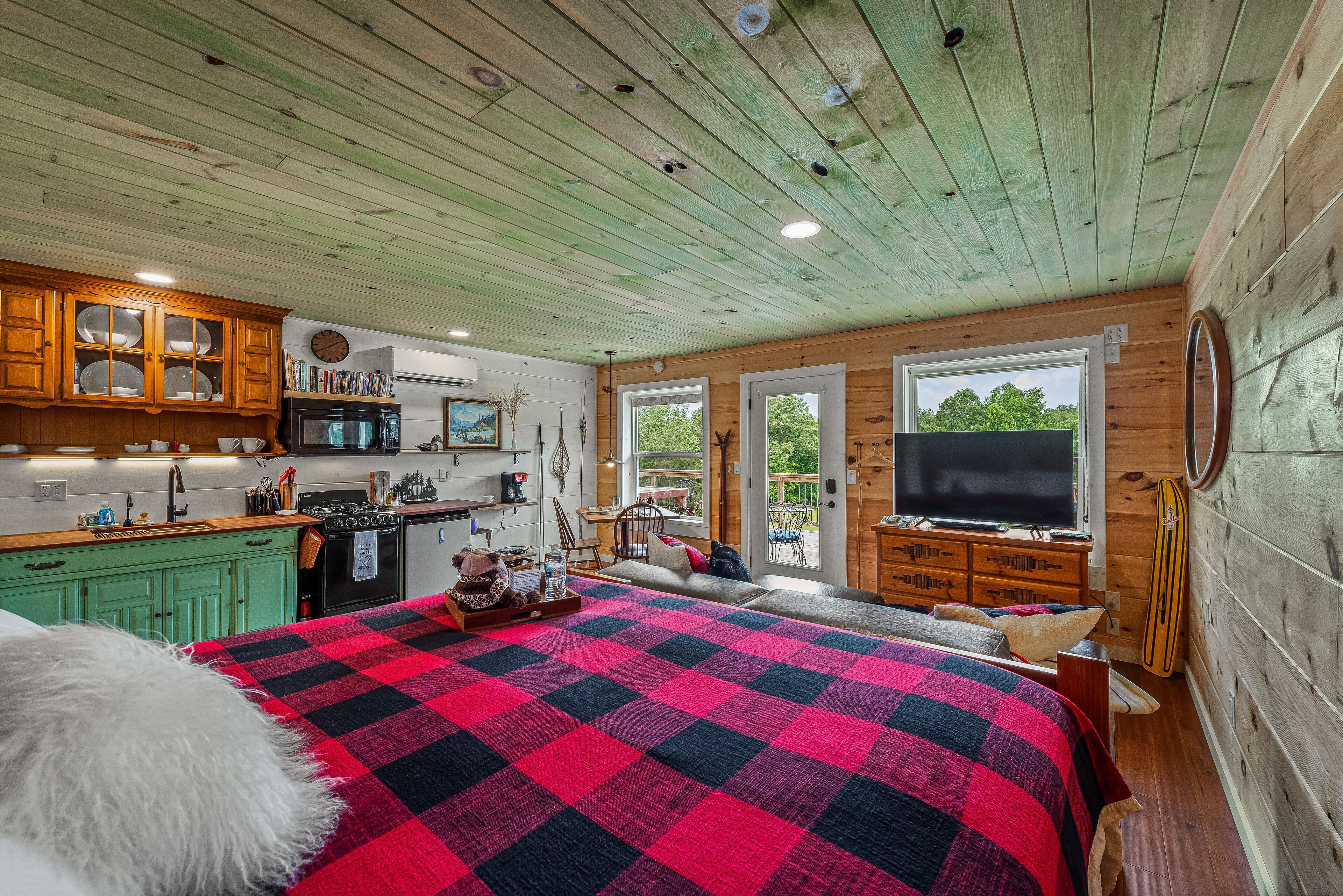 Un intérieur de chalet chaleureux avec un grand lit, des murs en bois, un coin cuisine et un téléviseur.