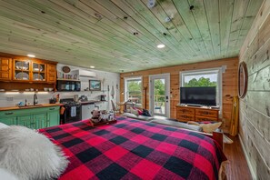 A cozy cabin interior with a large bed, wooden walls, a kitchen area, and a TV. - Wilderness Country Inn: Canada (Mentone)