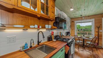 A kitchen with wooden cabinets, a sink, a stove, and a dining area with chairs.