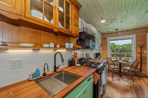 A kitchen with wooden cabinets, a sink, a stove, and a dining area with chairs. - Wilderness Country Inn: Canada (Mentone)