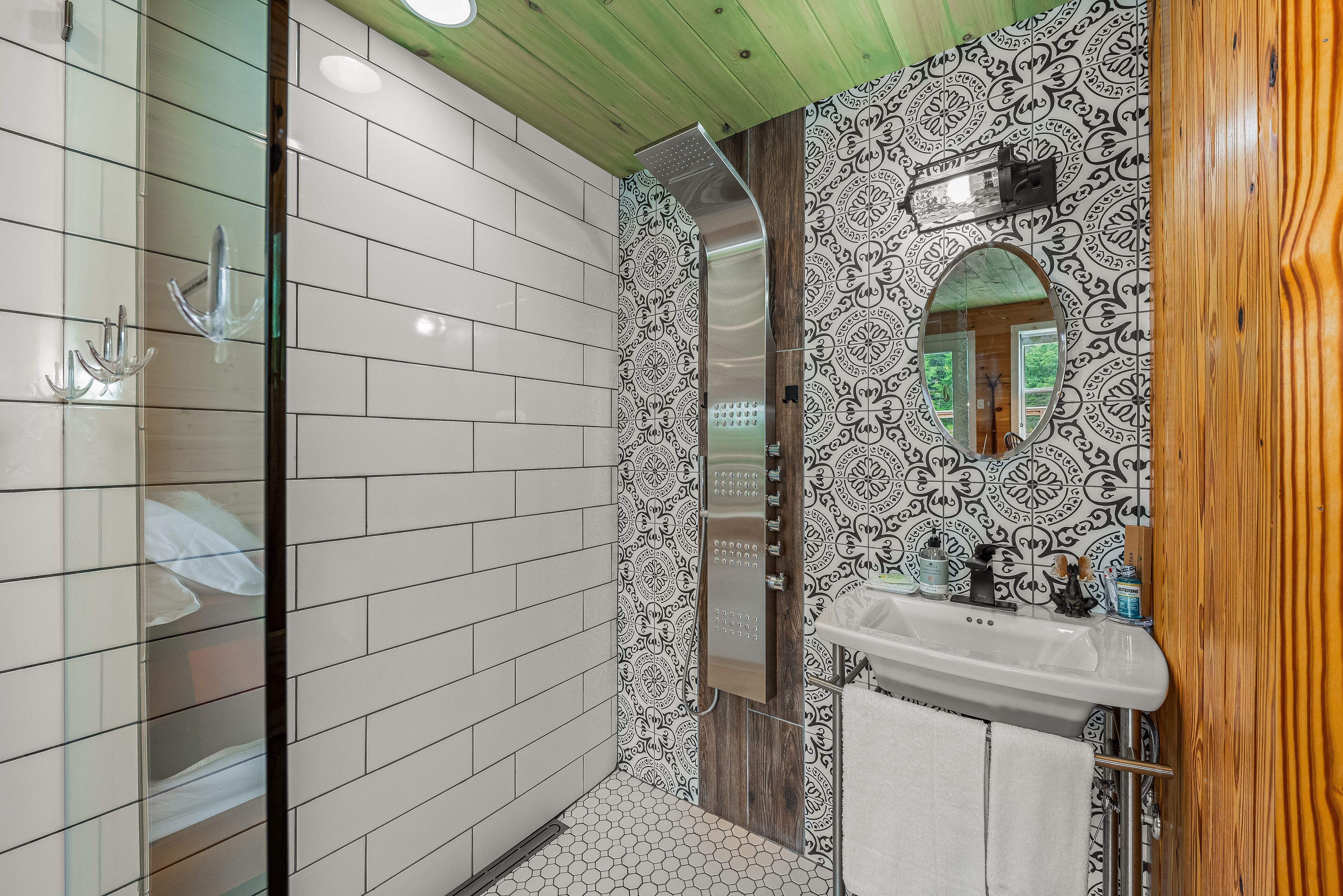 A bathroom with white tiled walls, a wooden vanity, a mirror, and a shower area.