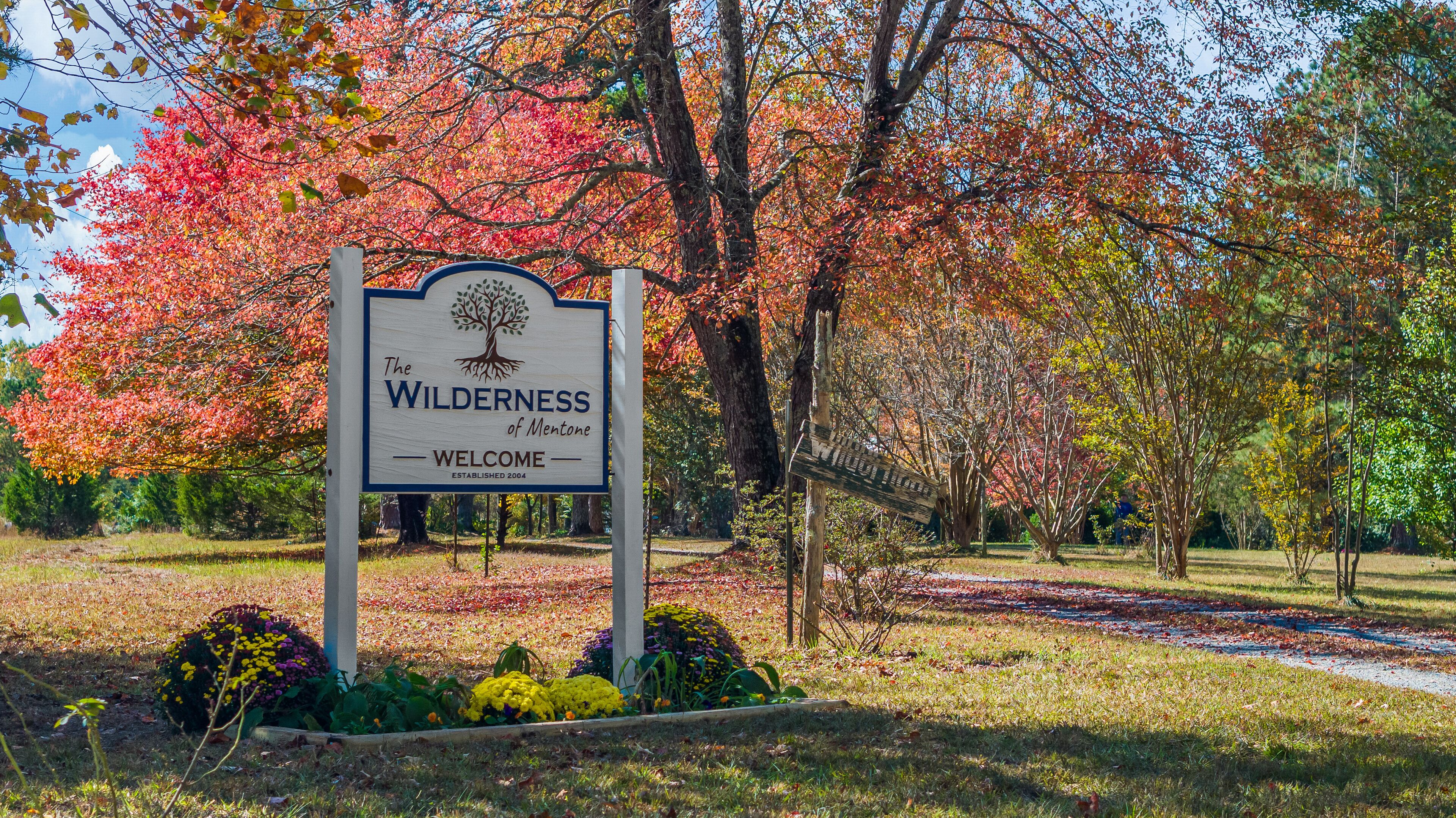 A sign welcoming visitors to The Wilderness of Mentor, established in 2004, surrounded by autumn foliage.