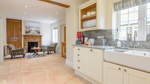 A kitchen with a fireplace, dining area, and a view of the street. - Sea Holly Cottage-UK11931 (Thornham, near Kings Lynn)