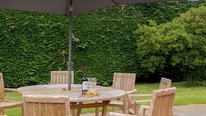 A round wooden table with chairs, an umbrella, and a bottle of wine. - Sea Holly Cottage-UK11931 (Thornham, near Kings Lynn)