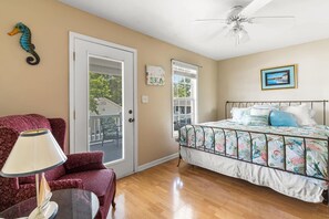 A bedroom with a bed, a chair, a lamp, a ceiling fan, and a door leading to a balcony.