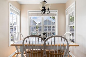 A dining area with a table and chairs, a chandelier, and large windows with blinds.